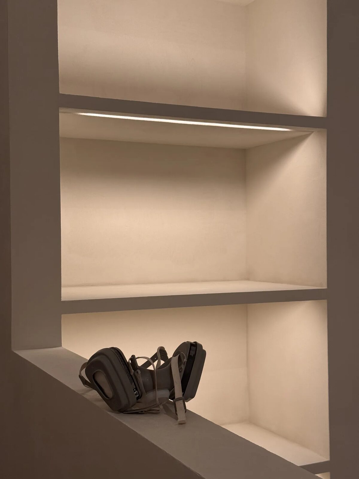 Plasterer's respirator resting in a lit Tadelakt niche during the Róhe installation